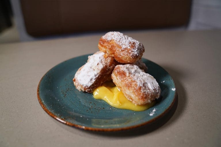 five beignets with lemon curd and powered sugar on a blue plate on a gray table in a restaurant in sandpoint idaho