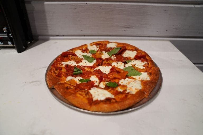 Margherita pizza with red sauce oven roasted tomatoes torn basil fresh burrata sea salt red pepper flakes and olive oil on a gray metal tray on a white counter in savory neighborhood grill in sandpoint idaho