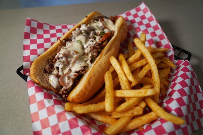 roasted beef italian grilled pork sausage pepperoni diced onion bell pepper provolone cheese and ranch in a hoagie roll next to french fries on a red and white checkered pattern paper in a black metal tray on a gray table in savory neighborhood grill in sandpoint idaho