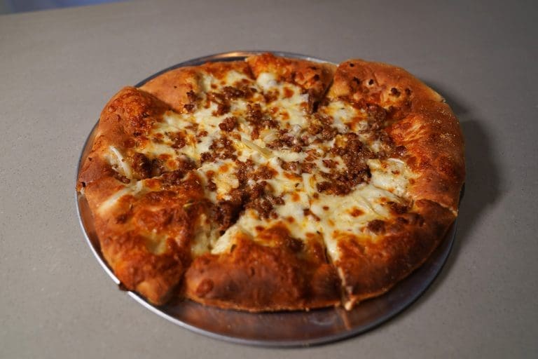 sausage and gennel pizza with white sauce cheese blend shaved fennel italian sausage garlic and shaved parmesan on a gray metal tray on a gray table in savory neighborhood grill in sandpoint idaho