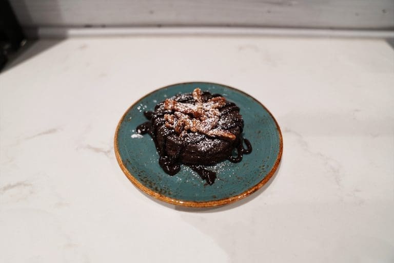 a flourless chocolate torte cake with toasted pecans and hot fudge on a blue plate on a white counter in savory neighborhood grill in sandpoint idaho